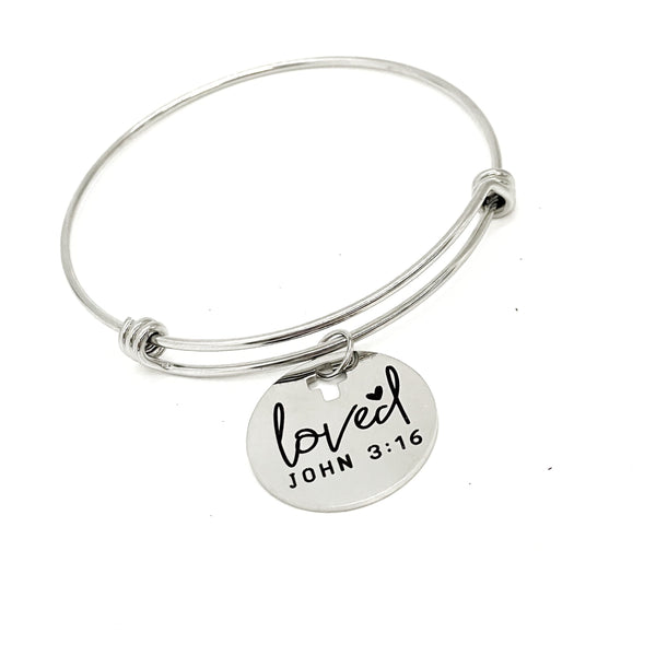 May include: A silver bangle bracelet with a round charm that says &#39;loved&#39; with a heart symbol and &#39;JOHN 3:16&#39;.